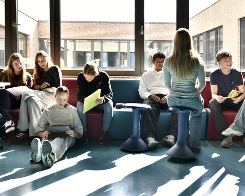 Schülerinnen und Schüler der Evangelischen Gesamtschule Werder sitzen auf einer großen Bank und am Boden und arbeiten an Laptops