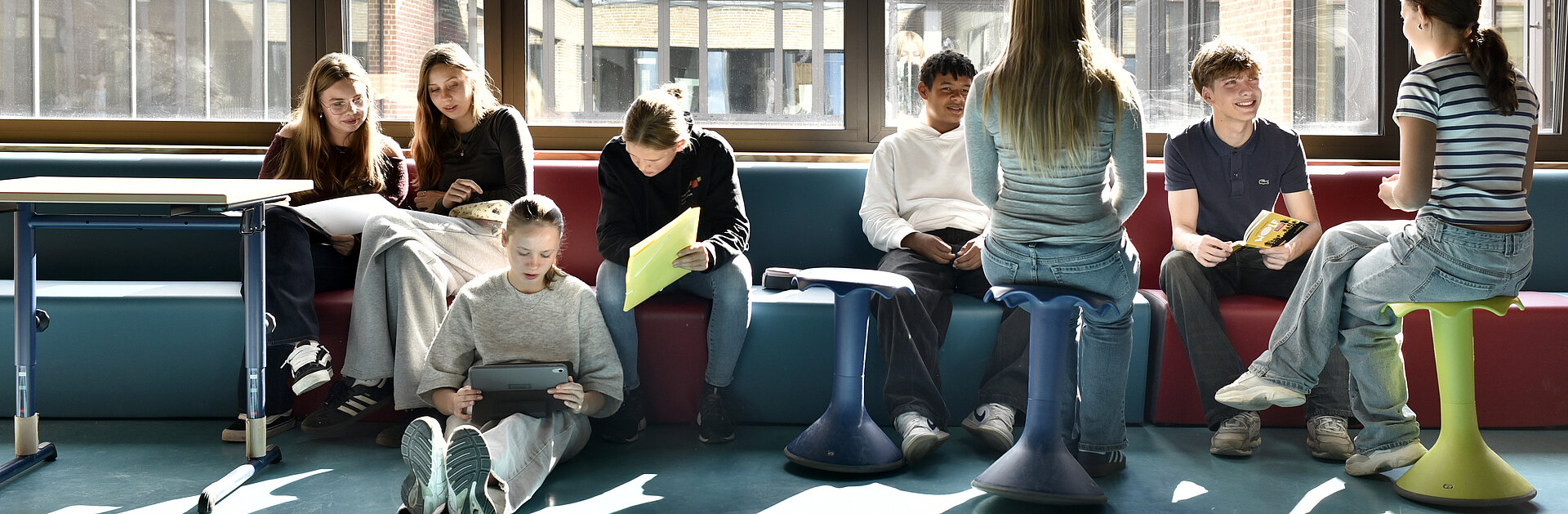 Schülerinnen und Schüler der Evangelischen Gesamtschule Werder sitzen auf einer großen Bank und am Boden und arbeiten an Laptops