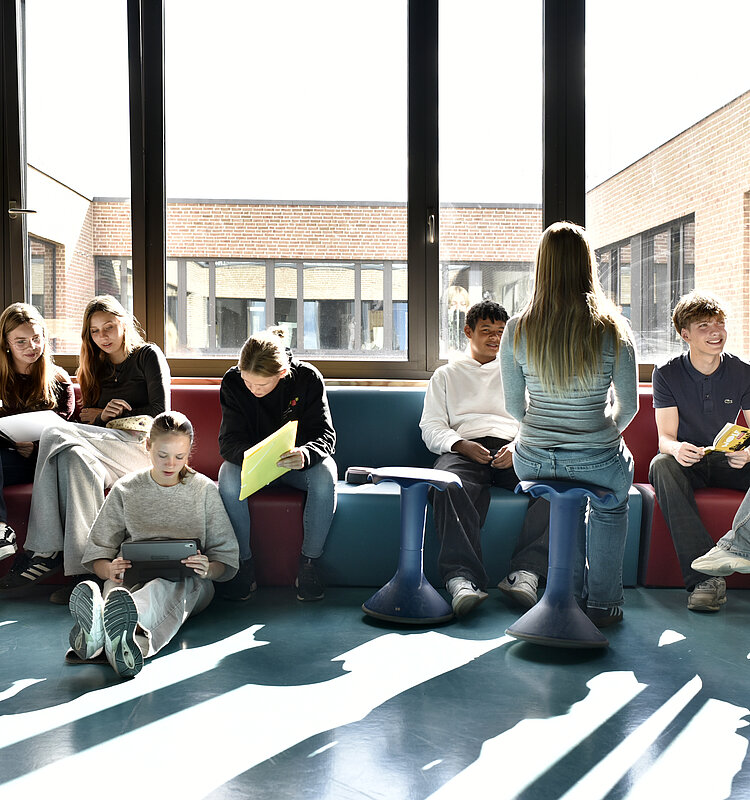 Schülerinnen und Schüler der Evangelischen Gesamtschule Werder sitzen auf einer großen Bank und am Boden und arbeiten an Laptops