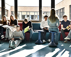 Schülerinnen und Schüler der Evangelischen Gesamtschule Werder sitzen auf einer großen Bank und am Boden und arbeiten an Laptops